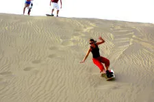 Girl sandboarding down large sand dunes near Huacachina oasi
